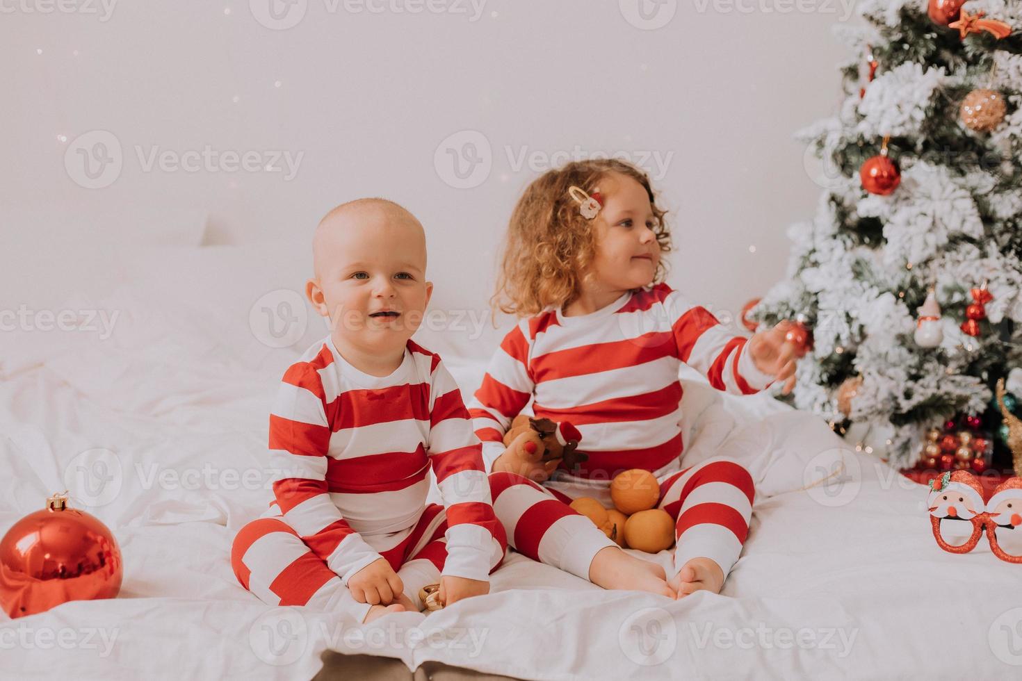 bambini nel rosso e bianca pigiama mangiare Natale dolci seduta nel letto. fratello e sorella, ragazzo e ragazza Condividere i regali. Natale mattina. stile di vita. spazio per testo. alto qualità foto