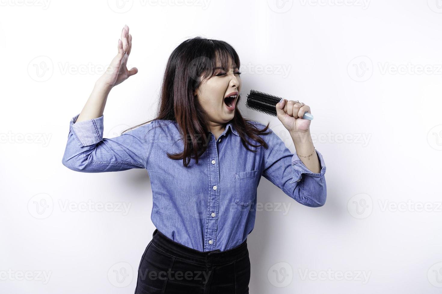 ritratto di spensierato asiatico donna, avendo divertimento karaoke, cantando nel microfono mentre in piedi al di sopra di bianca sfondo foto