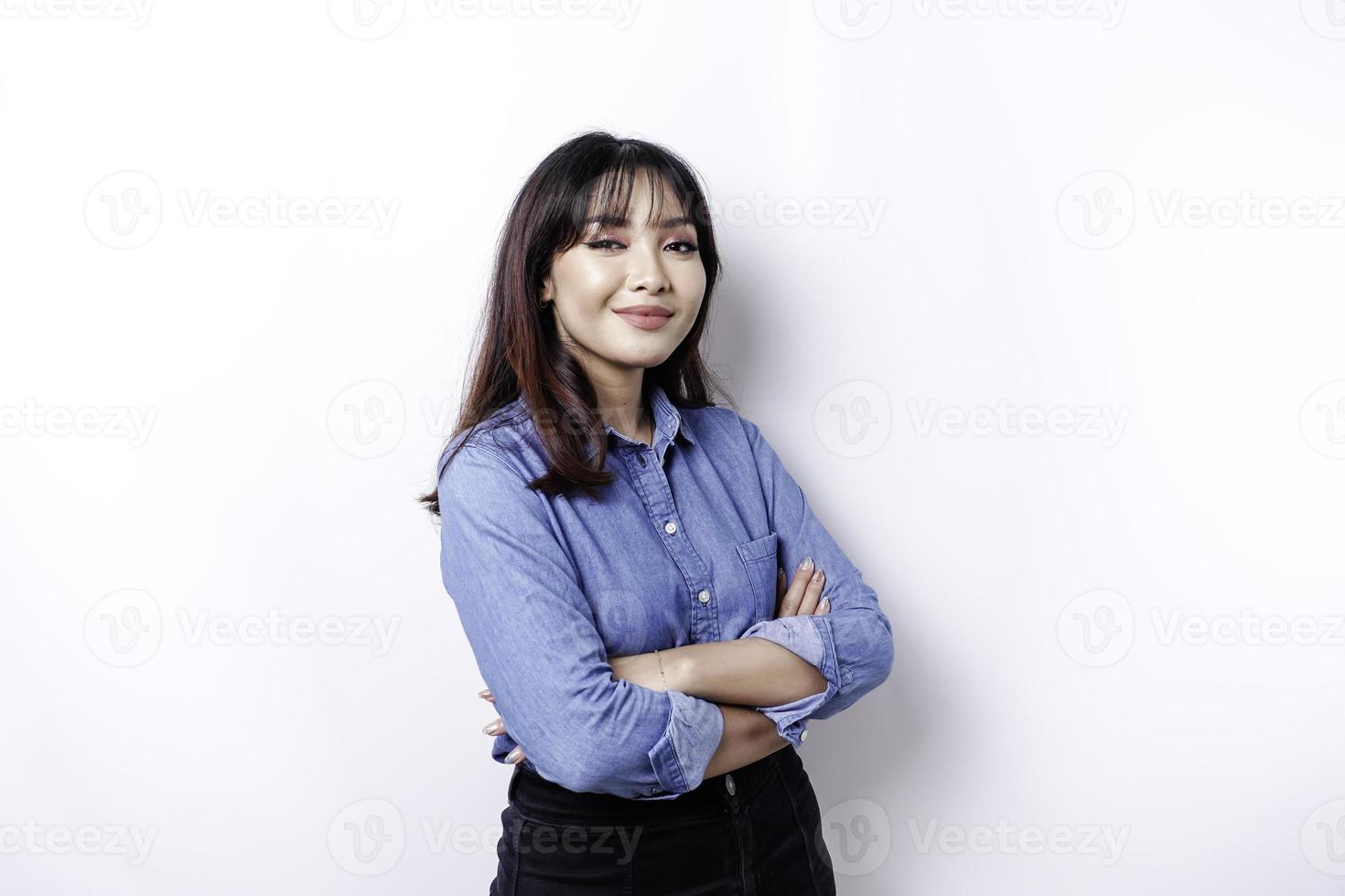 ritratto di un' fiducioso sorridente asiatico donna indossare blu camicia in piedi con braccia piegato e guardare a il telecamera isolato al di sopra di bianca sfondo foto