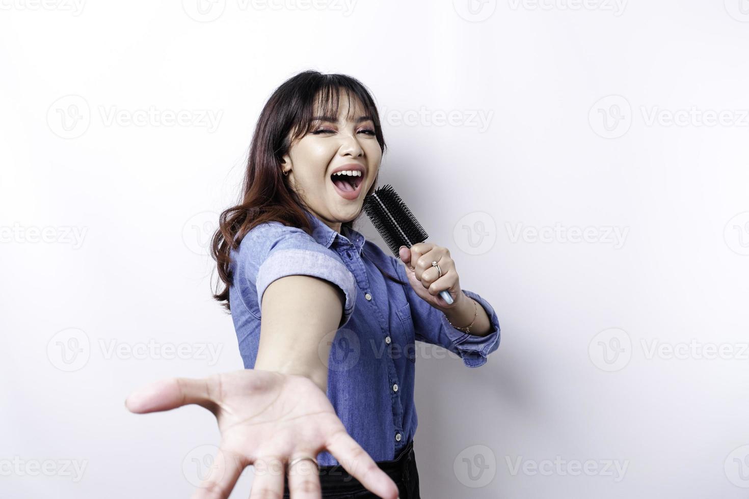 ritratto di spensierato asiatico donna, avendo divertimento karaoke, cantando nel microfono mentre in piedi al di sopra di bianca sfondo foto