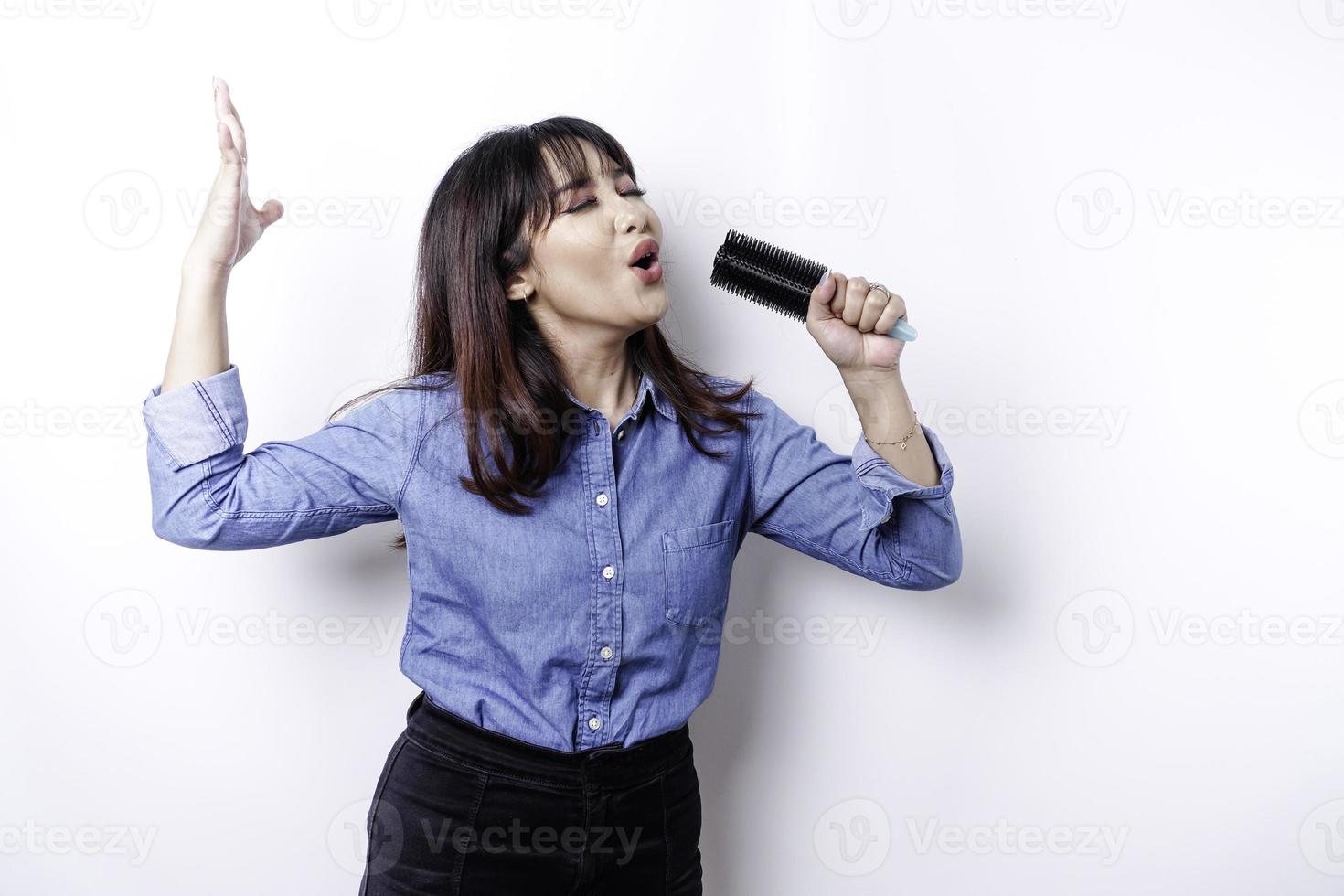 ritratto di spensierato asiatico donna, avendo divertimento karaoke, cantando nel microfono mentre in piedi al di sopra di bianca sfondo foto