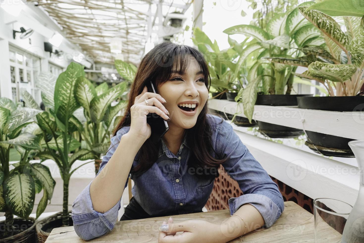 un' contento asiatico donna nel un' ristorante, indossare un' blu camicia e Tenere sua Telefono foto