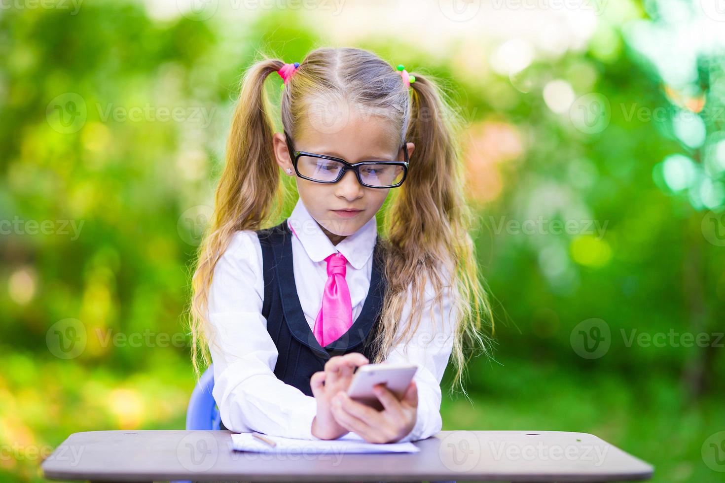 adorabile poco scuola ragazza a un' tavolo con Appunti e matite, indietro per scuola all'aperto foto