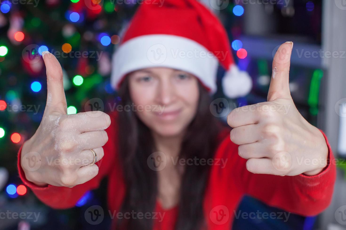 giovane donna nel Natale cappello sollevato pollici su a casa foto