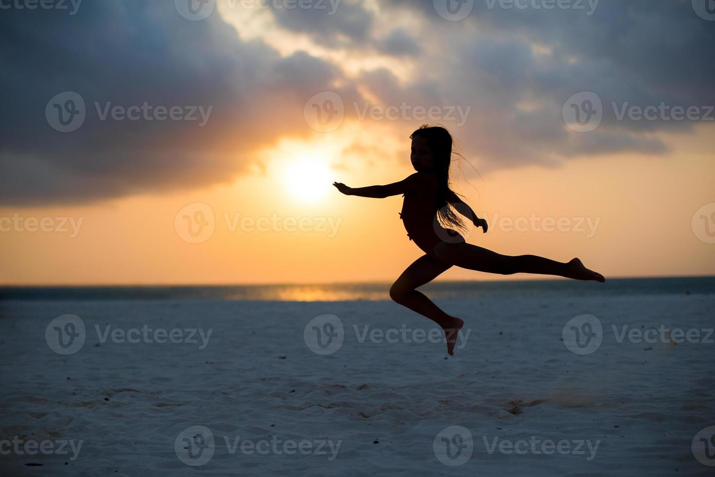 silhouette di adorabile poco ragazza su bianca spiaggia a tramonto foto