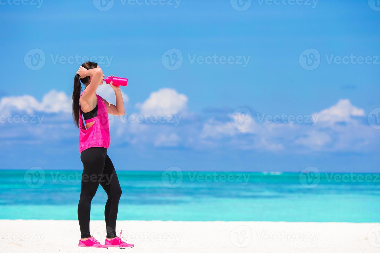 in forma giovane donna bevanda acqua su bianca spiaggia foto