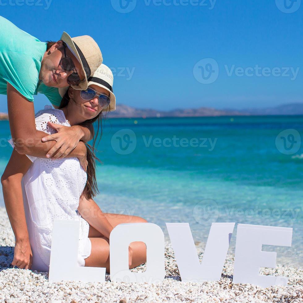 giovane bellissimo famiglia seduta su il spiaggia con parola amore foto