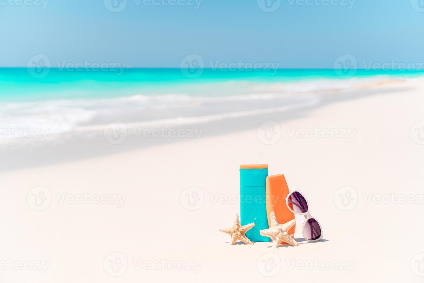 crema solare bottiglie, occhiali, stella marina e occhiali da sole su bianca sabbia spiaggia sfondo oceano foto