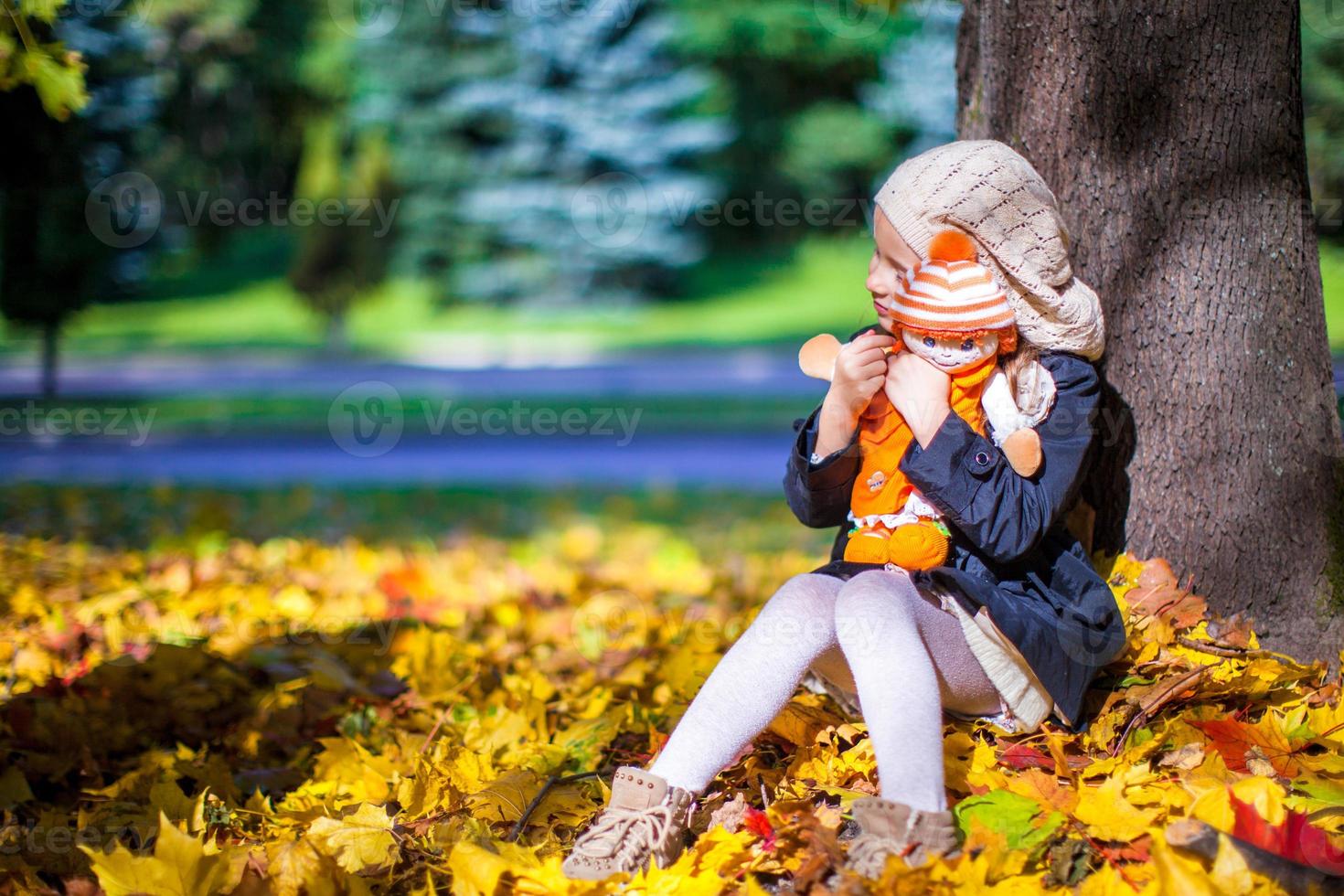 bella moda ragazza si siede sotto un' acero albero con Bambola su soleggiato autunno giorno foto