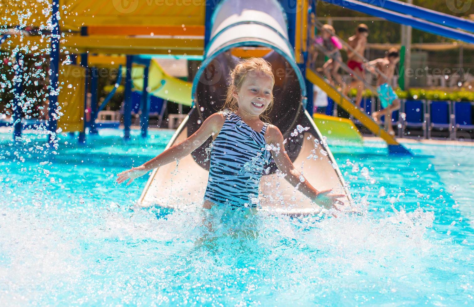 poco ragazza su acqua diapositiva a Parco acquatico durante estate vacanza foto