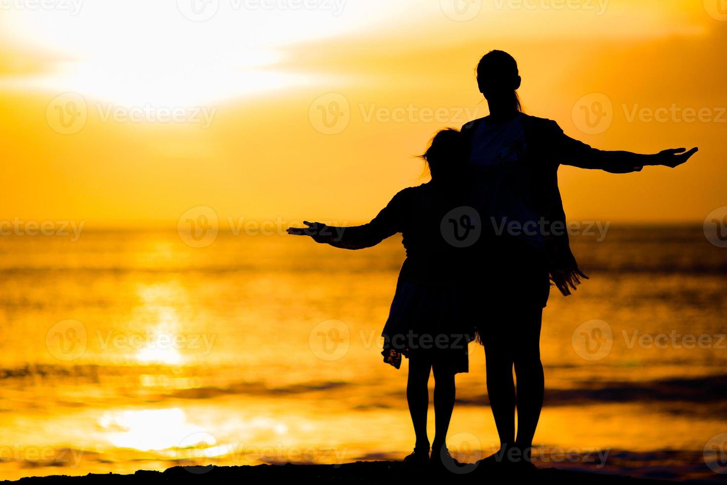 poco ragazza e contento madre silhouette nel il tramonto a il spiaggia foto