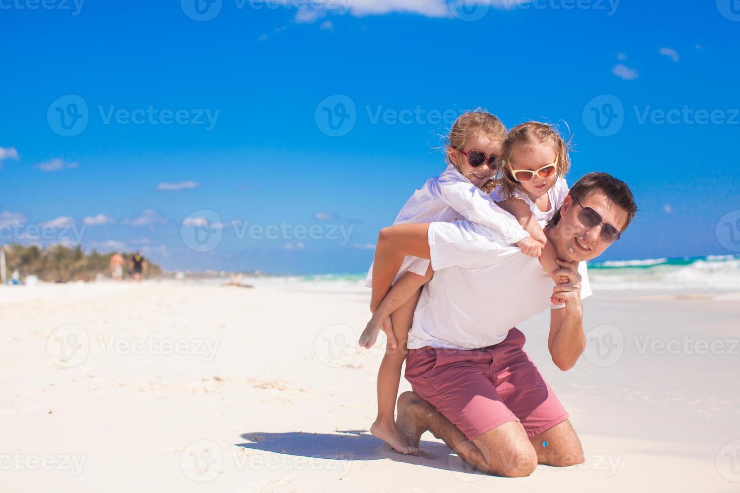 giovane contento padre e poco figlie avendo divertimento su bianca spiaggia nel soleggiato giorno foto