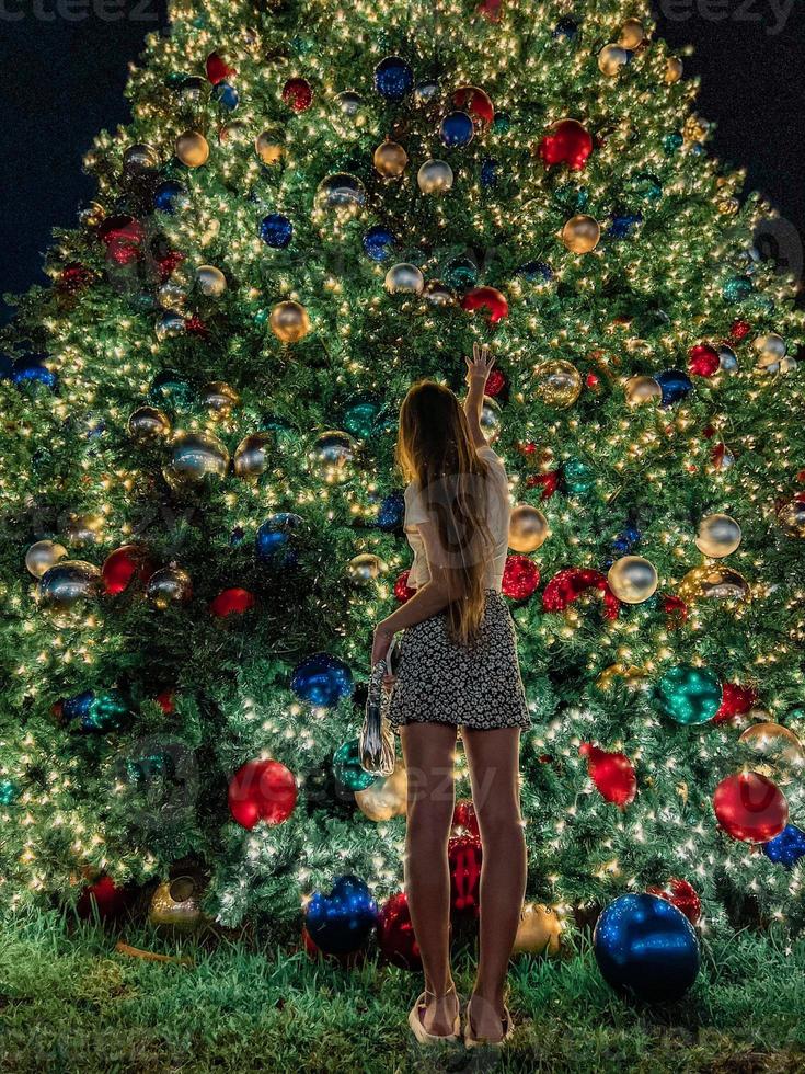 giovane ragazza su il sfondo di il Natale albero nel miami. bellissimo Natale albero a il popolare la zona a natale vigilia e luci foto