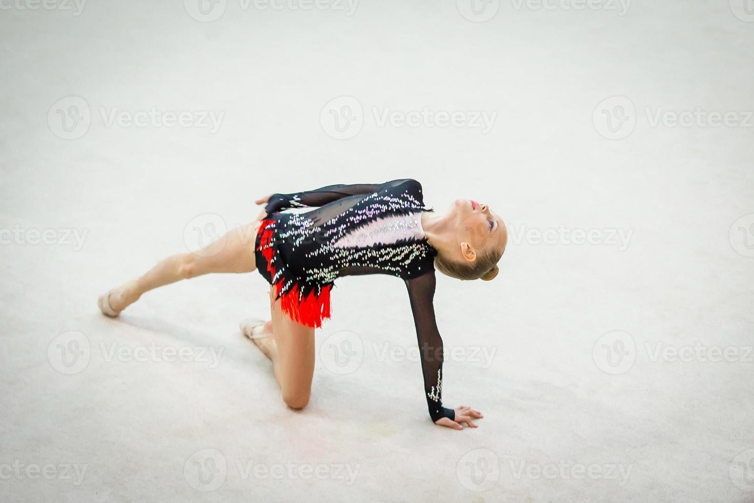 bellissimo poco attivo ginnasta ragazza con sua prestazione su il tappeto foto