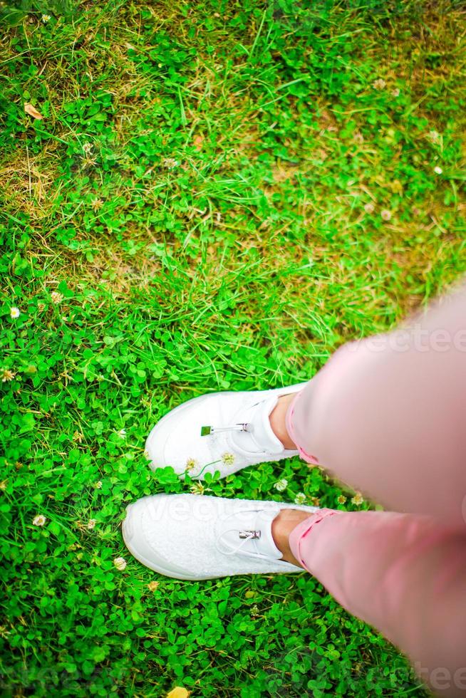 avvicinamento di femmina gambe nel scarpe da ginnastica su il erba all'aperto nel il parco. foto