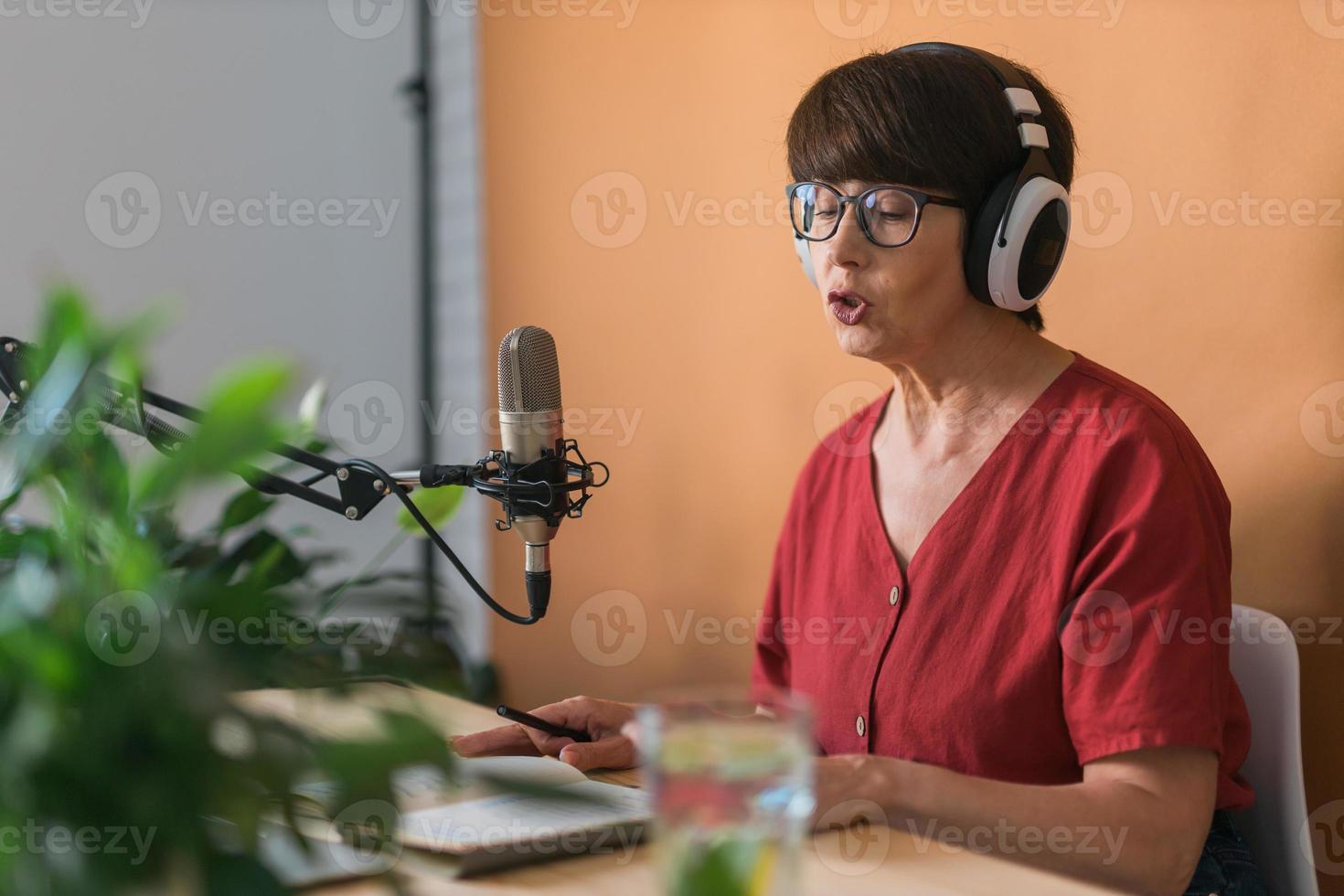 ritratto di maturo donna indossare cuffie e parlando a in linea Radio stazione - Podcast e trasmissione concetto foto