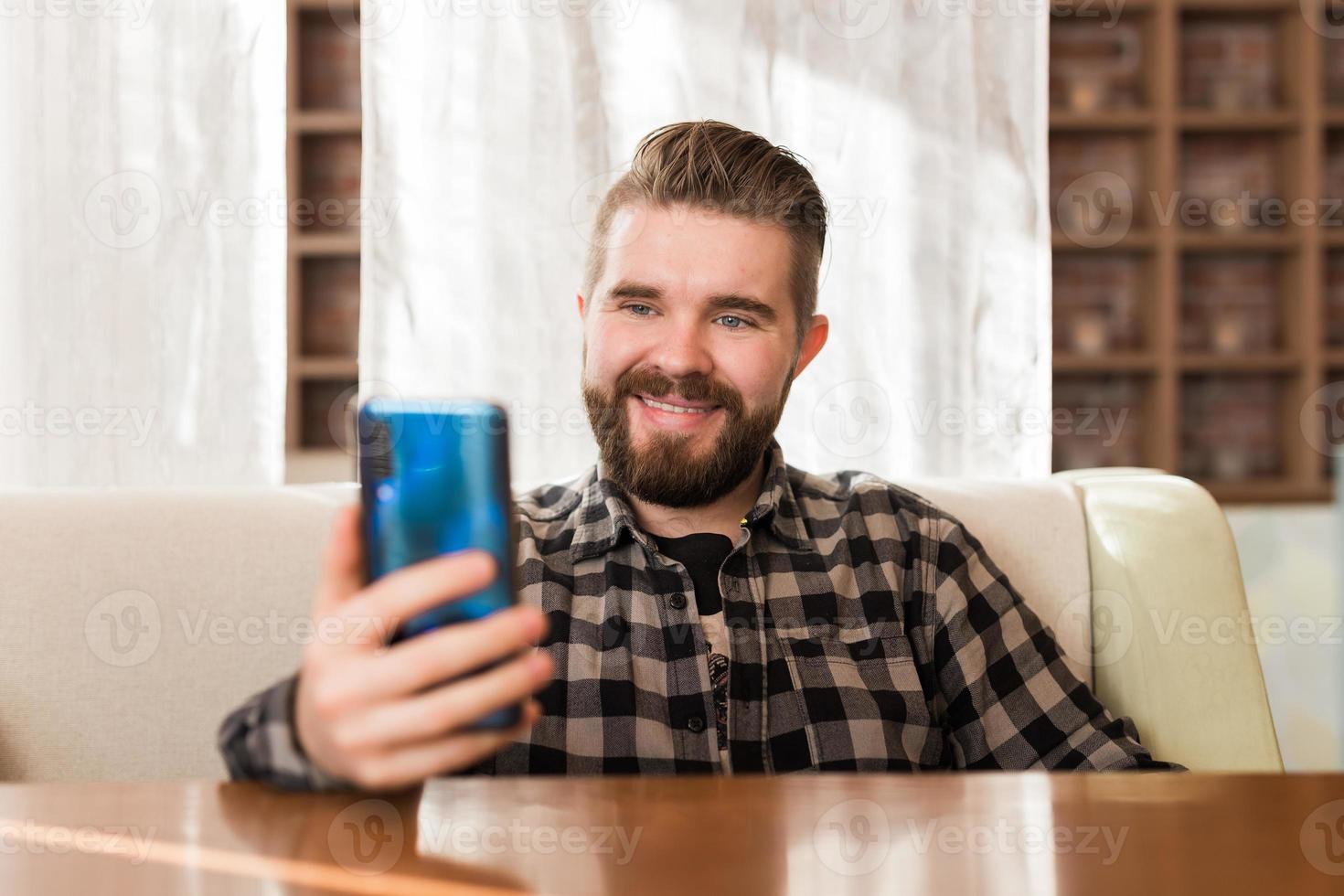 vicino su giovane uomo seduta a caffè bar e utilizzando video chiamata a partire dal smartphone per saluto e parlando con amici e famiglia per nuovo normale e salutare stile di vita concetto foto