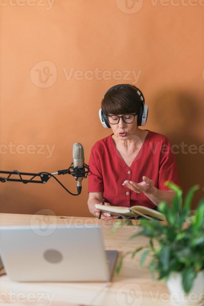 ritratto di maturo donna indossare cuffie e parlando a in linea Radio stazione - Podcast e trasmissione concetto foto