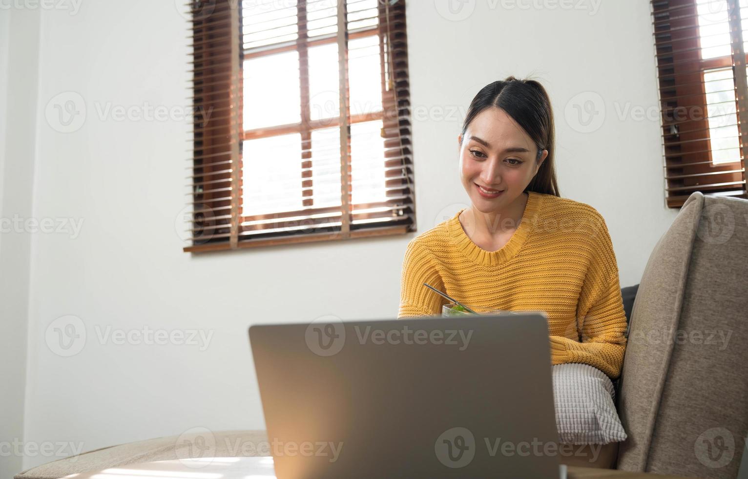 persone rilassare a casa e benessere stile di vita. giovane adulto asiatico donna mangiare insalata e utilizzando il computer portatile computer per Guardando in linea film su Internet. foto