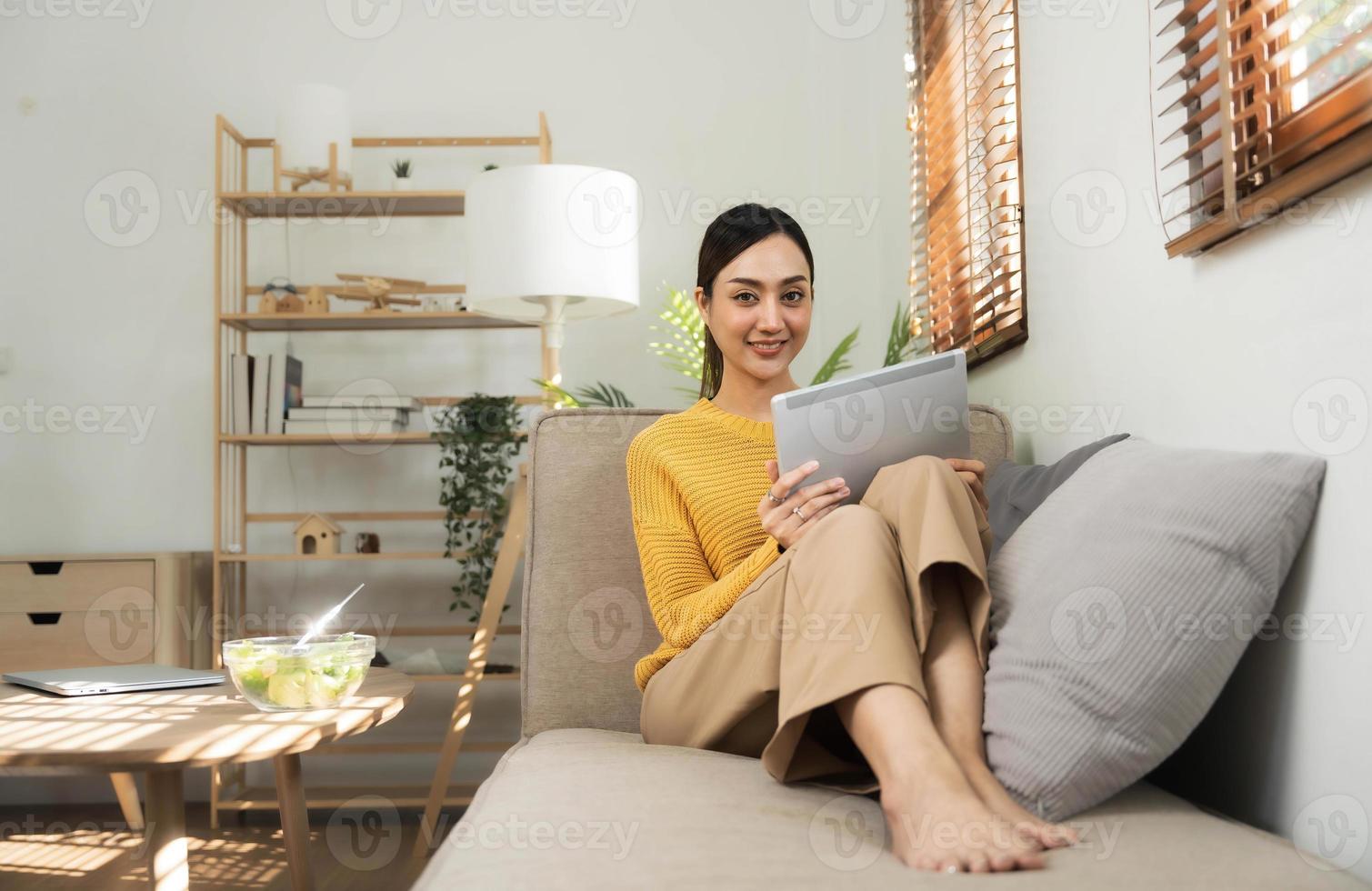 ritratto di un' giovane contento femmina seduta su il divano e Lavorando su progetto, Guardando film su computer portatile, studiando, blog, riposo e chat in linea. foto