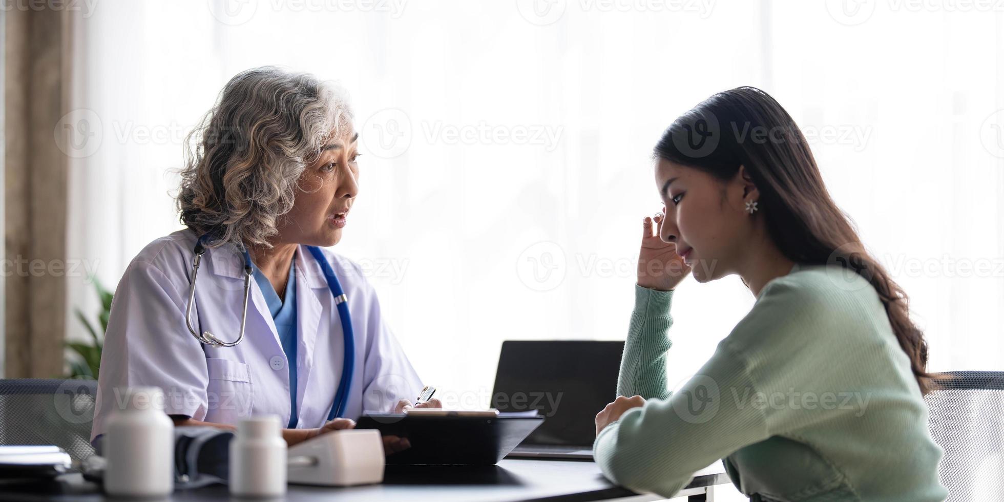 donna anziano medico è lettura medico storia di femmina paziente e A proposito di con sua durante consultazione nel un' Salute clinica. medico nel laboratorio cappotto seduta dietro a un' il computer portatile nel ospedale ufficio. foto