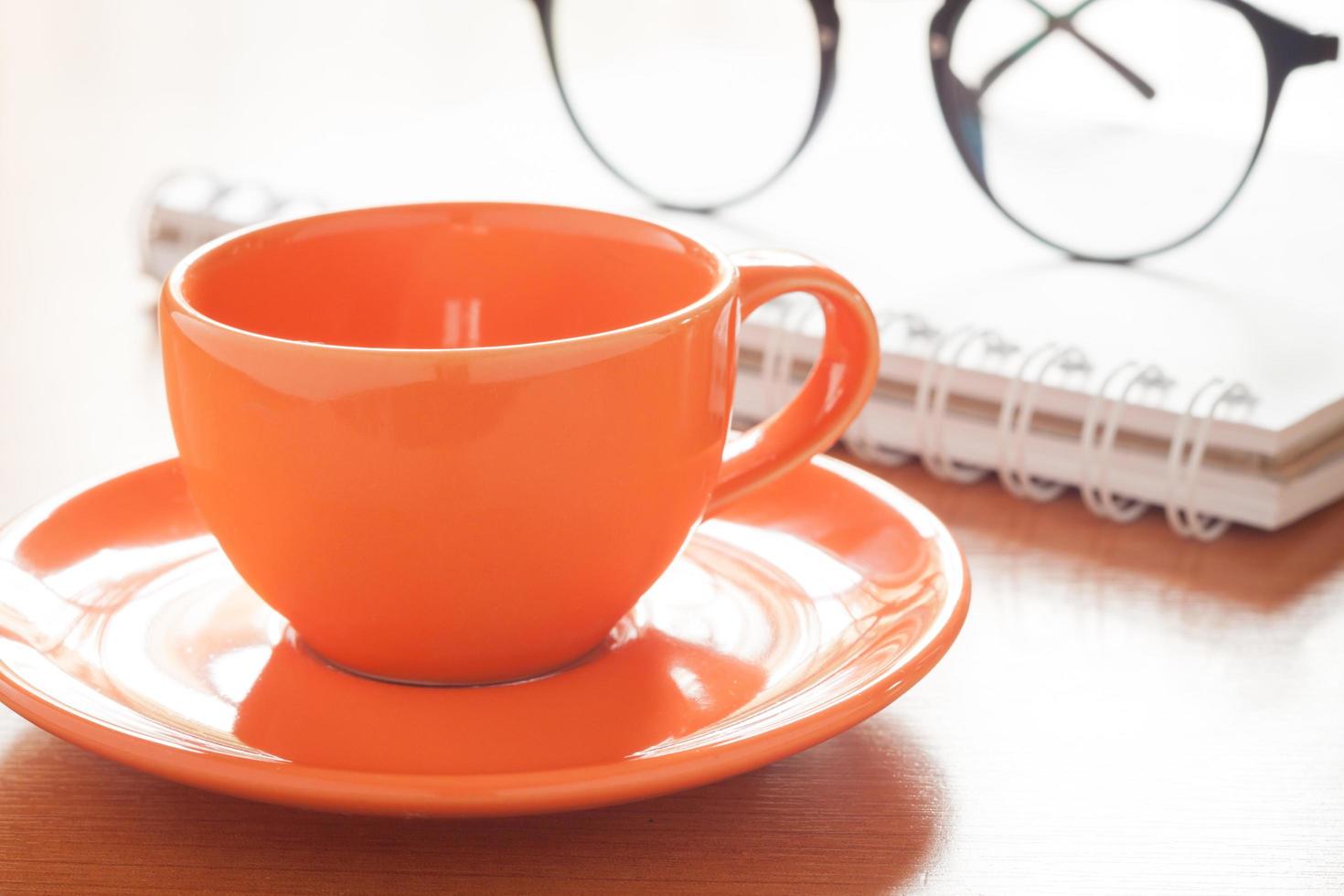 primo piano di una tazza di caffè con un taccuino e occhiali da vista foto