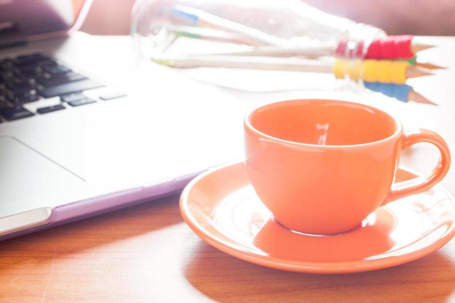 tazza di caffè accanto a un computer portatile su una scrivania foto