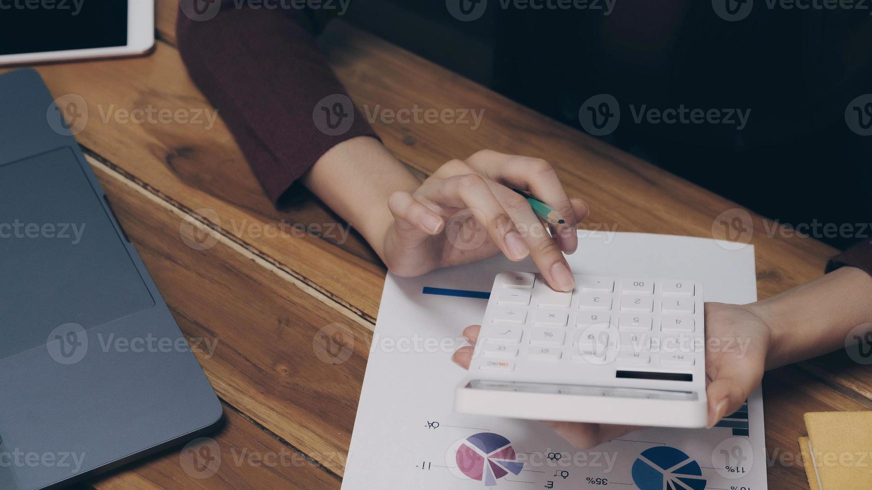donna d'affari utilizzando calcolatrice e laptop alla scrivania in ufficio foto