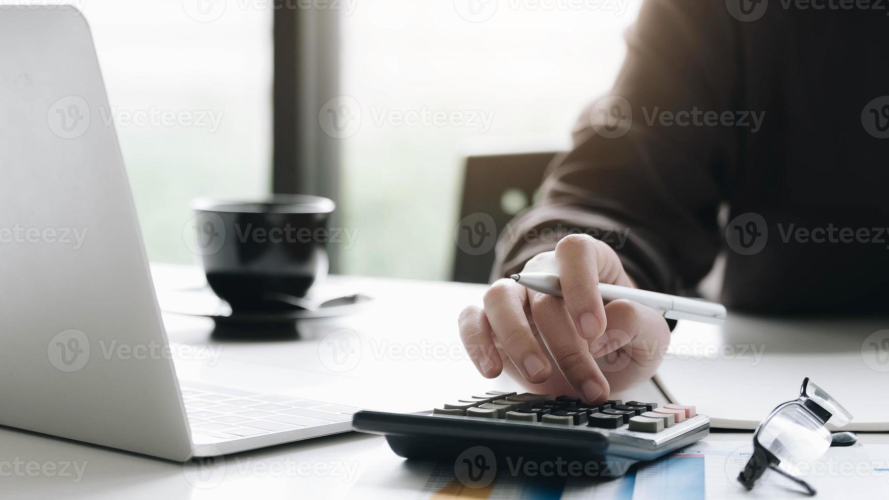 donna d'affari utilizzando calcolatrice e laptop alla scrivania in ufficio foto