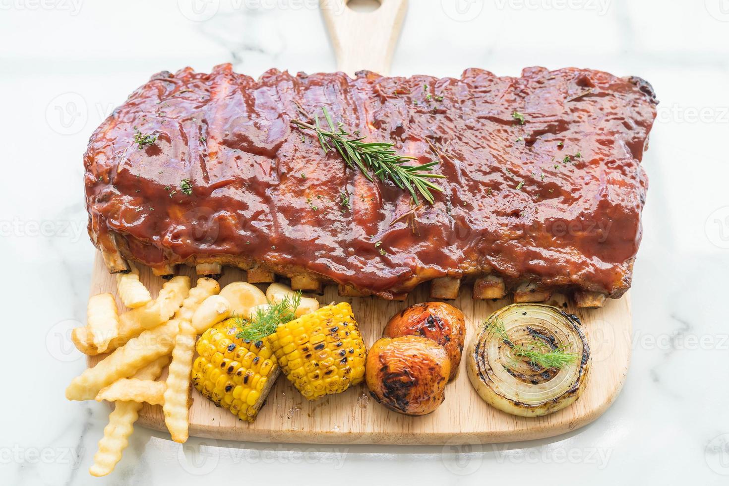 costolette barbecue alla griglia con verdure e patatine fritte sul tagliere di legno foto