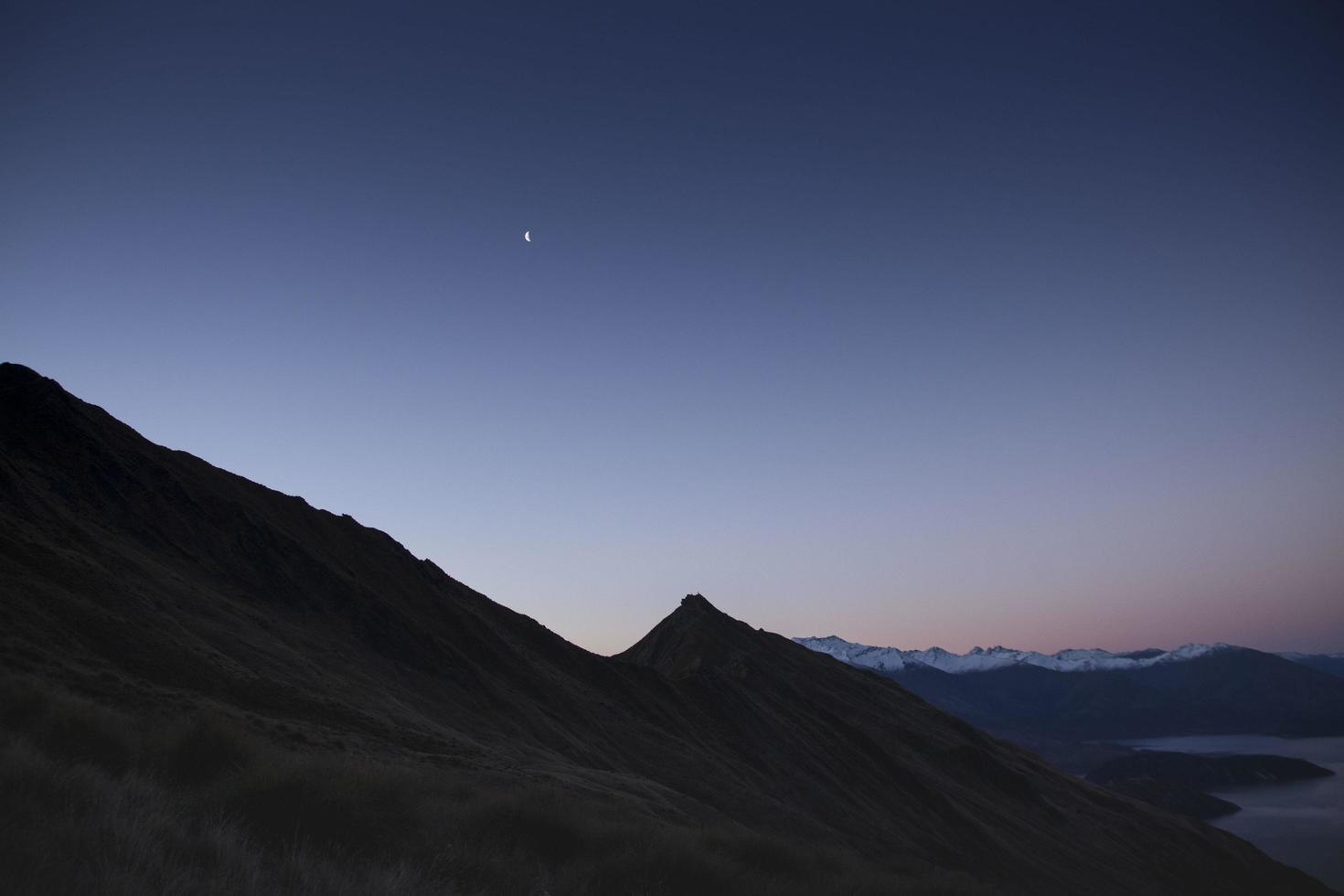 scheggia di luna sulle montagne al crepuscolo foto