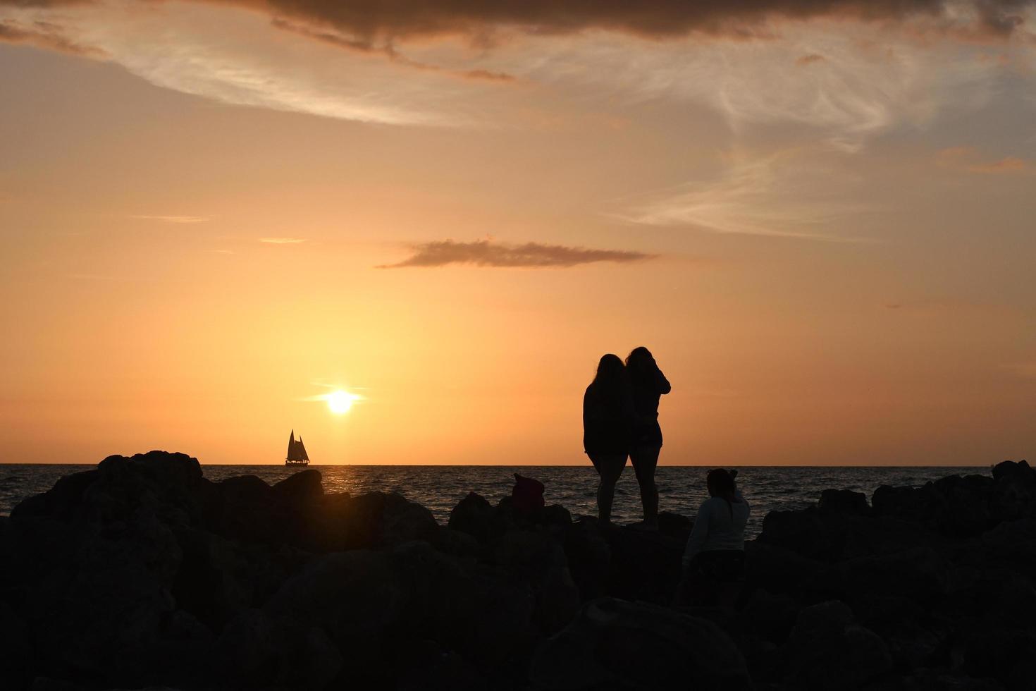 silhouette di due persone in piedi sulla spiaggia rocciosa durante il tramonto foto