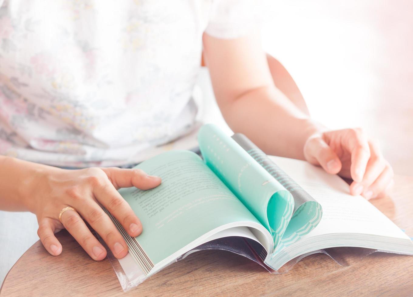 primo piano di una persona che legge un libro a un tavolo foto