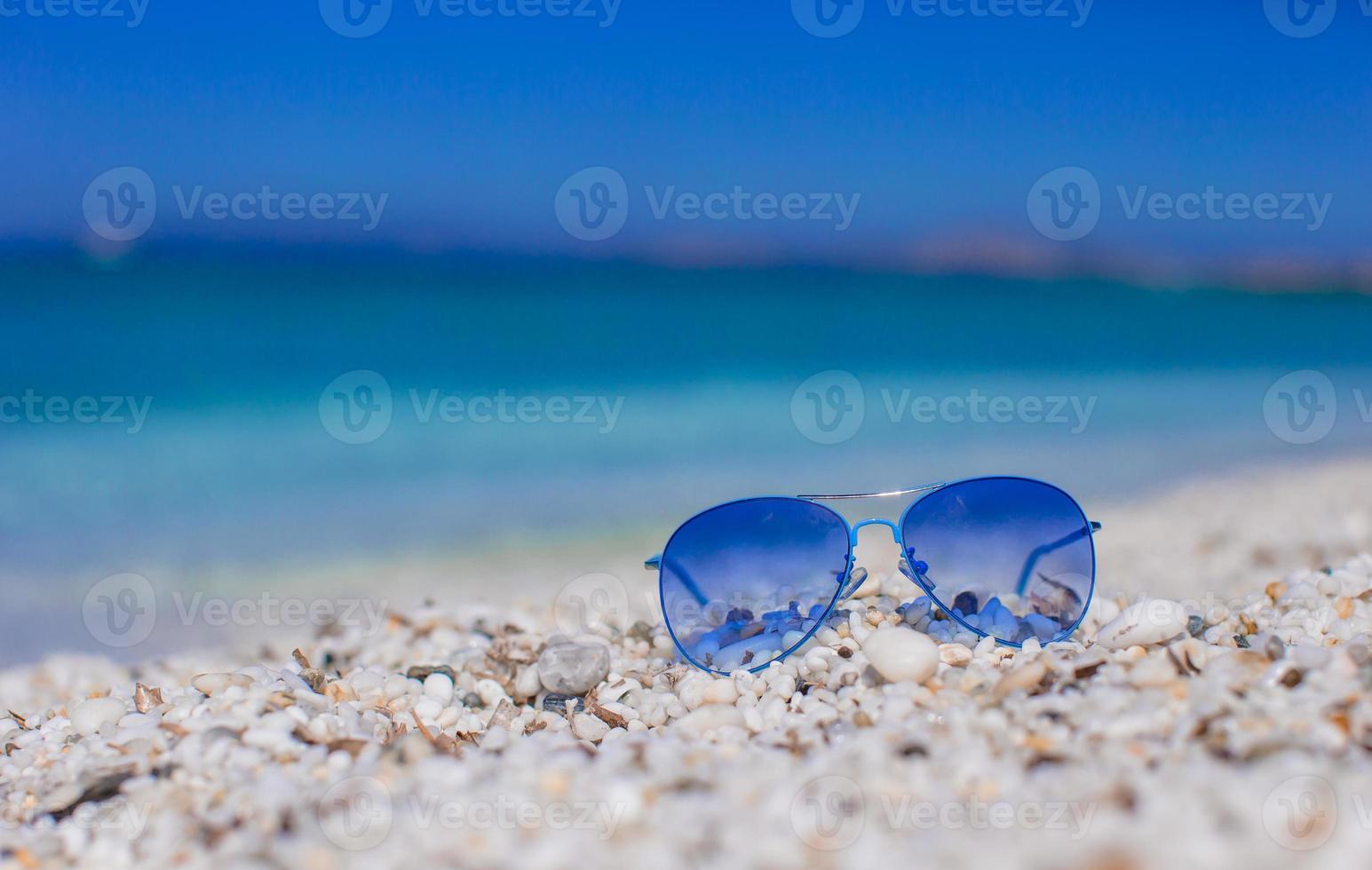 vicino su di colorato blu occhiali da sole su tropicale spiaggia foto