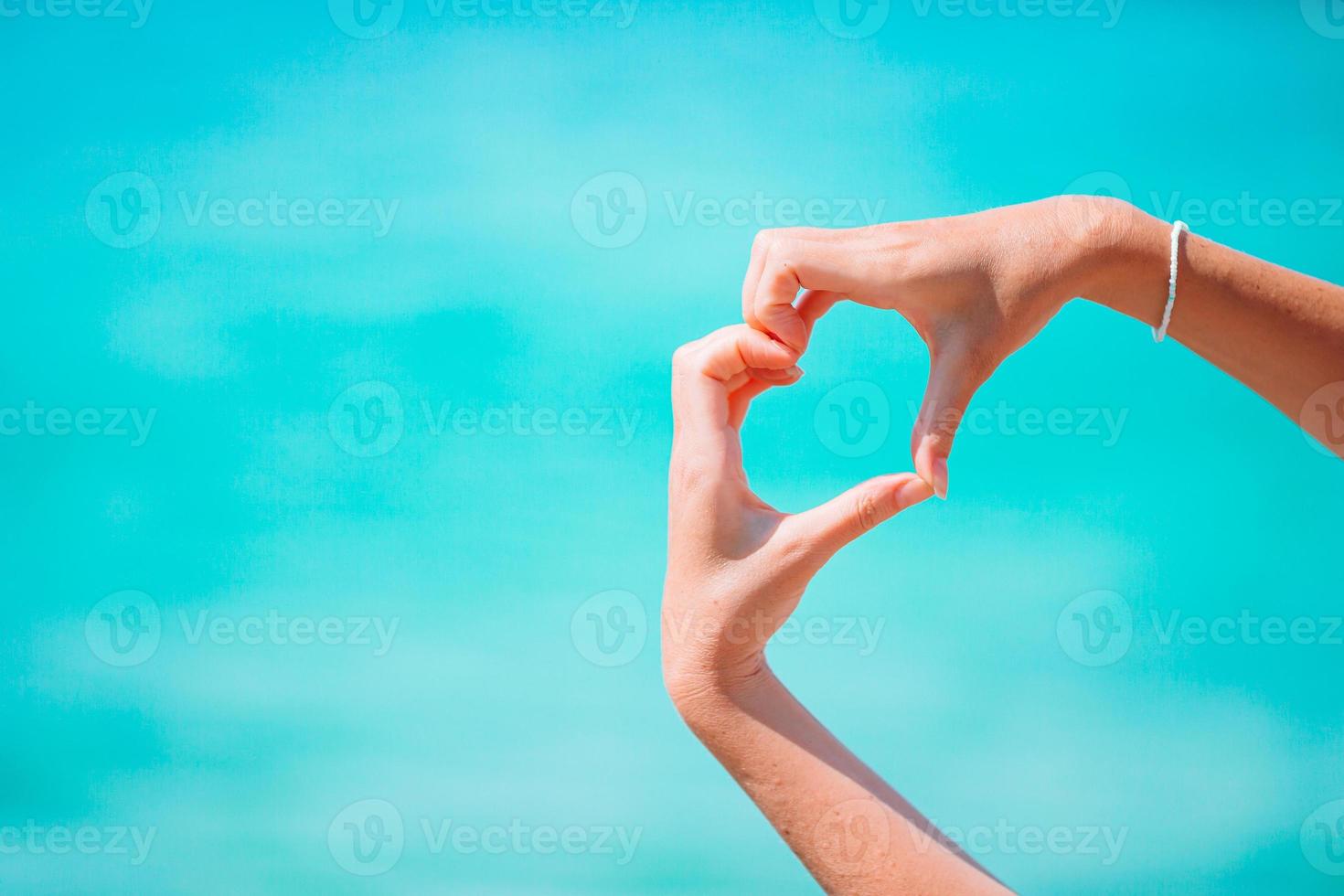 femmina mani nel il modulo di cuore contro il turchese mare foto