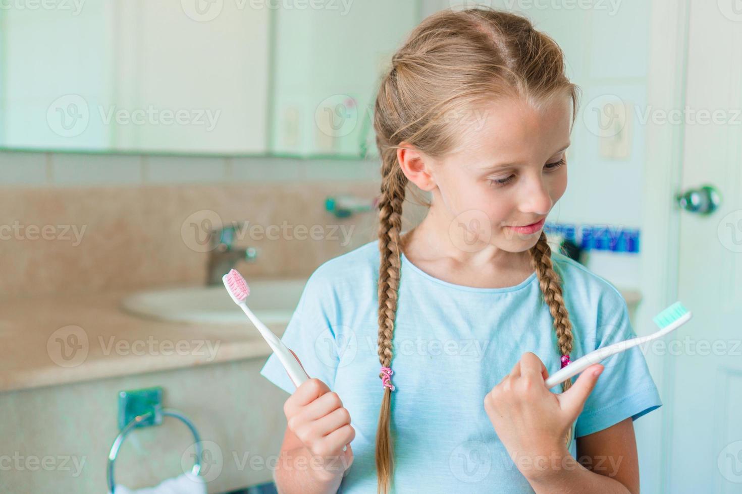 poco adorabile ragazza spazzolatura denti nel il bagno. Perfetto bianco come la neve Sorridi di poco ragazza foto