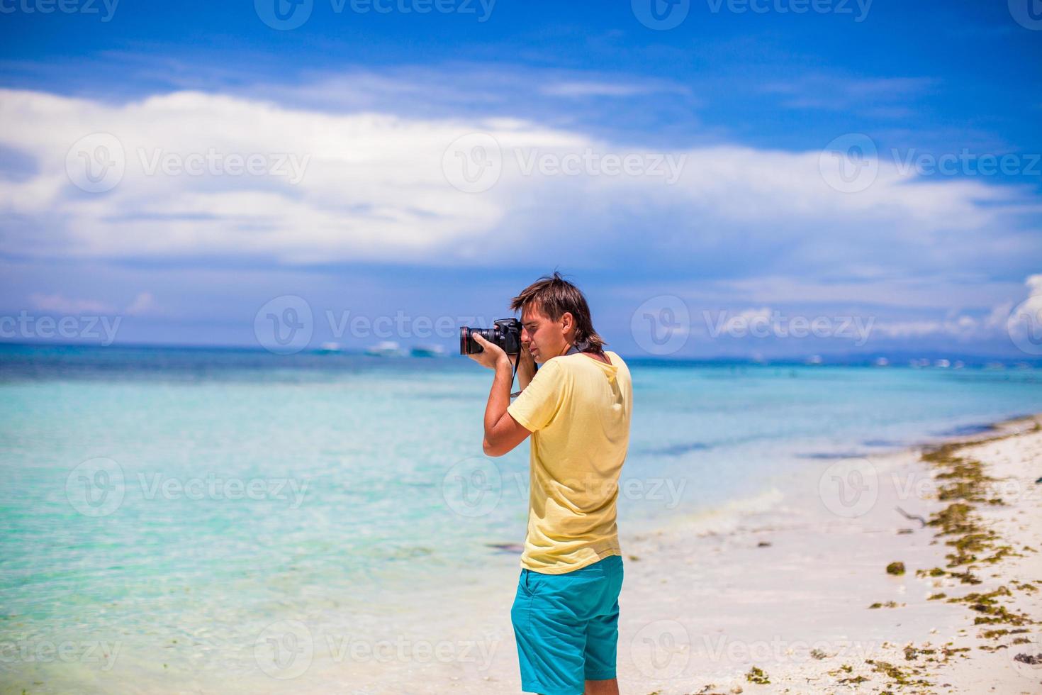 giovane uomo Fotografare con telecamera nel il suo mani su un' tropicale spiaggia foto