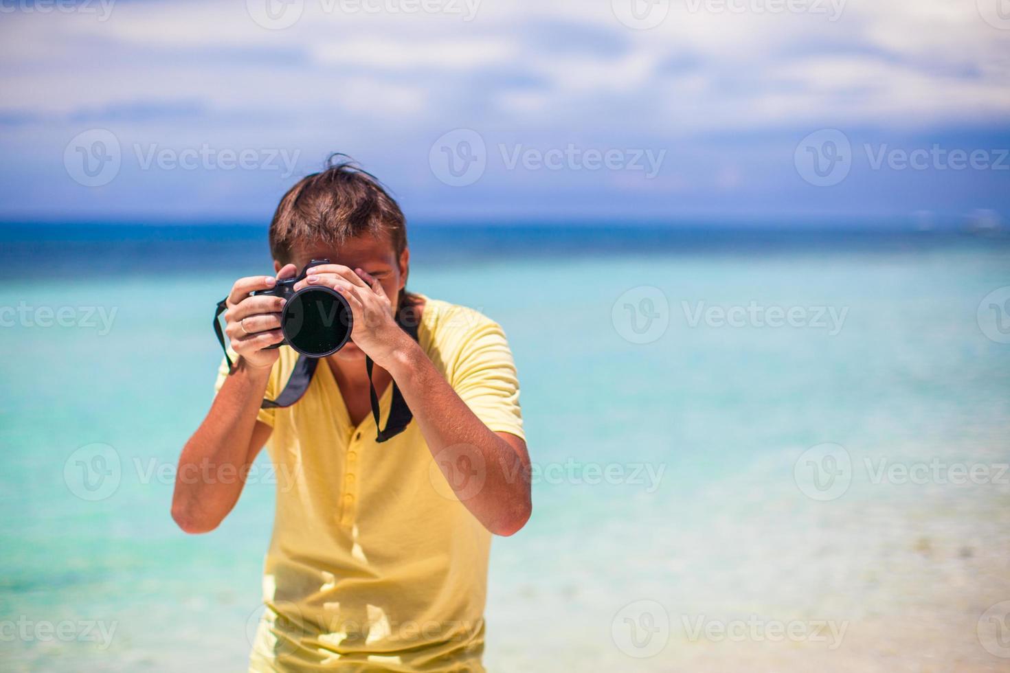 giovane uomo Fotografare con telecamera nel il suo mani su un' tropicale spiaggia foto