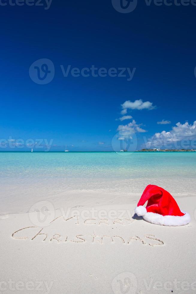 allegro Natale scritto su tropicale spiaggia bianca sabbia con natale cappello foto