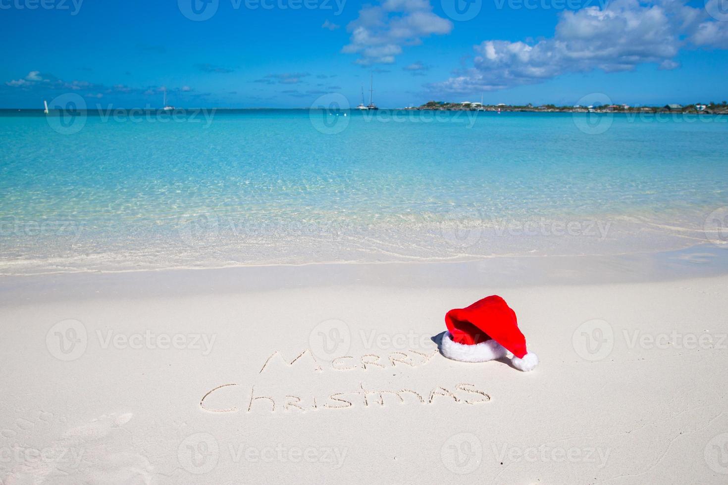allegro Natale scritto su tropicale spiaggia bianca sabbia con natale cappello foto