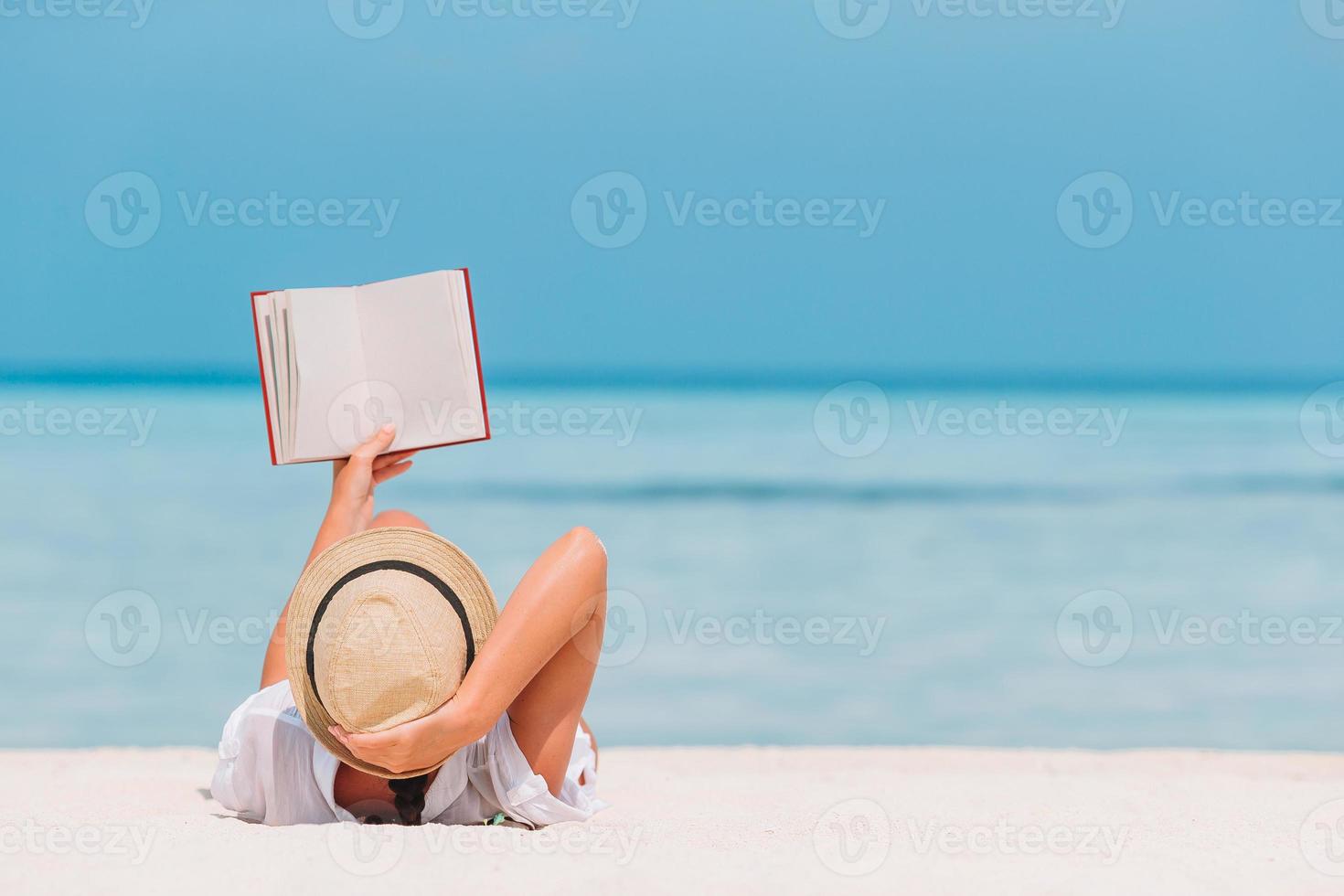 ritratto di un' giovane donna rilassante su il spiaggia, lettura un' libro foto