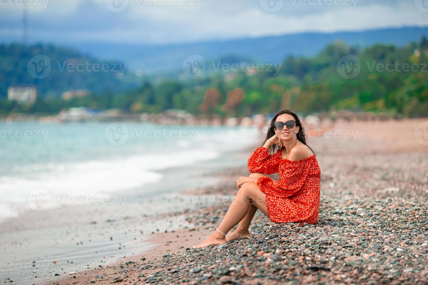 giovane contento donna su il spiaggia con montagna Visualizza foto