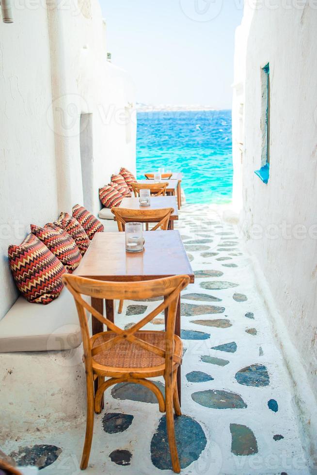 panchine con cuscini nel un' tipico greco all'aperto bar nel mykonos con sorprendente mare Visualizza su Cicladi isole foto
