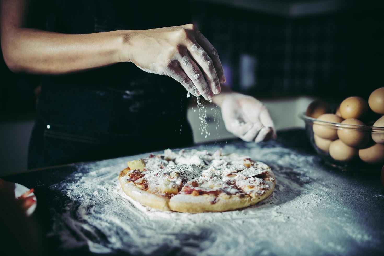 mani dello chef che versano farina sulla pasta cruda foto