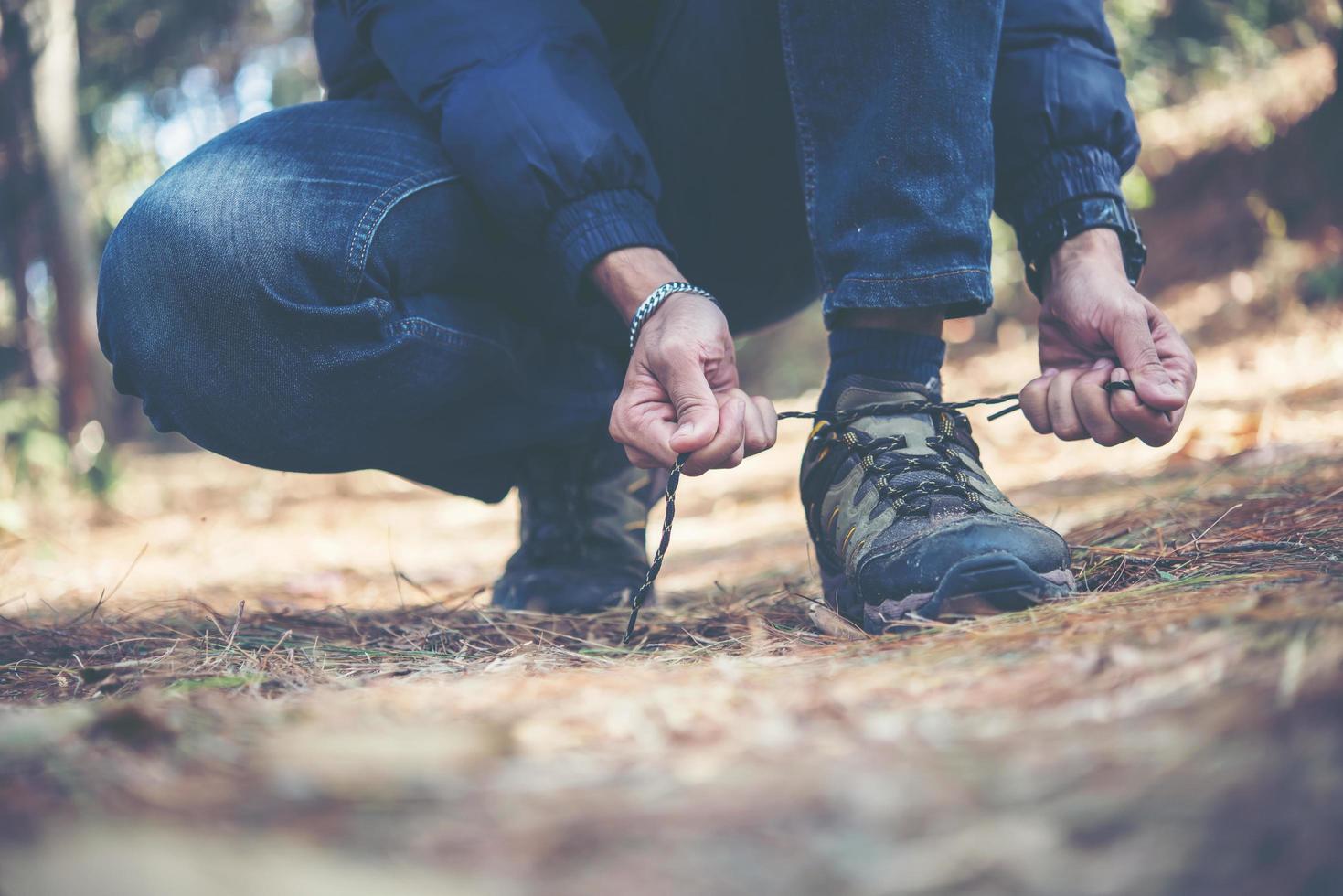 giovane escursionista allaccia i lacci delle scarpe mentre è in viaggio con lo zaino in spalla nella foresta foto