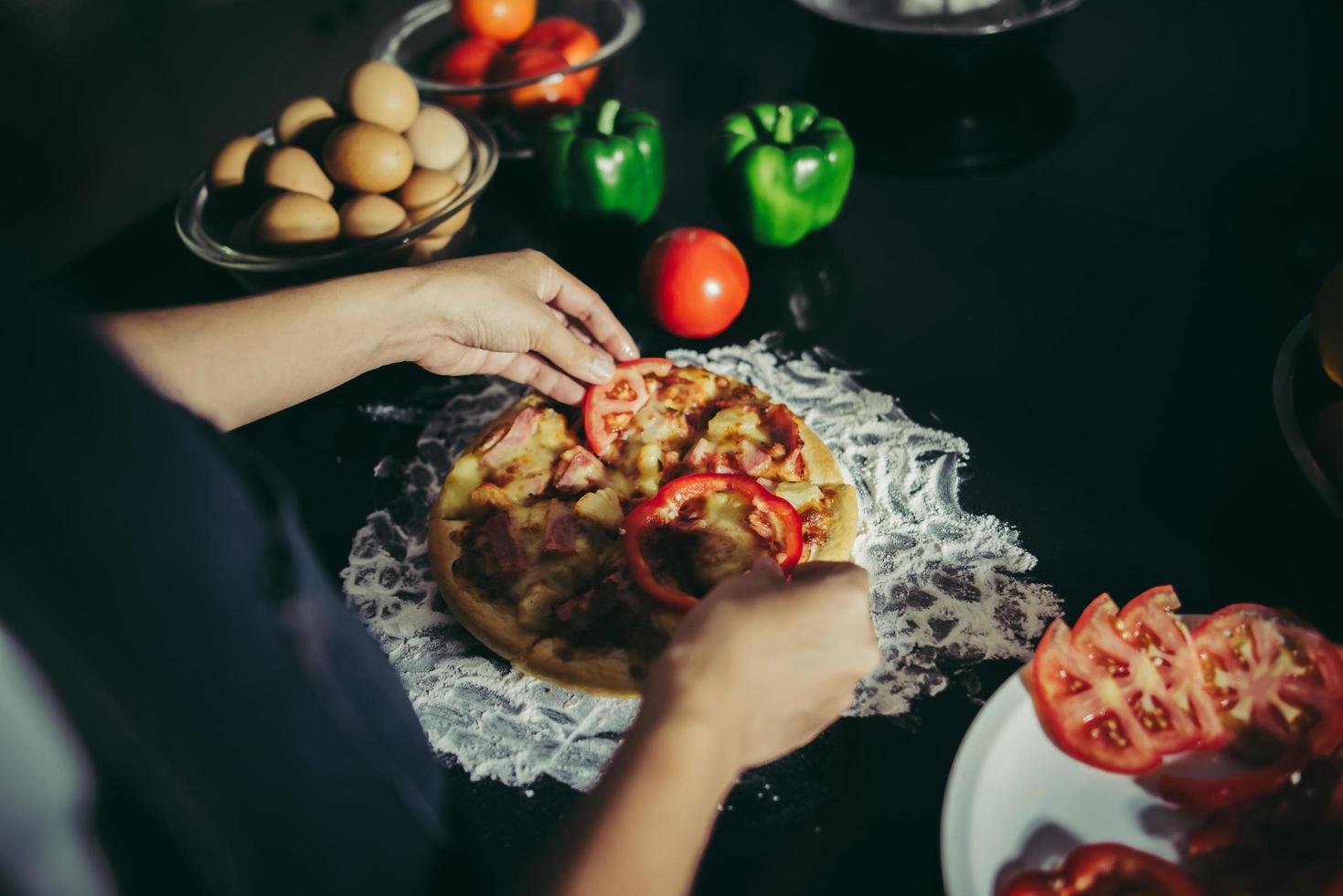 primo piano di una donna che mette condimenti sulla pizza fatta in casa foto