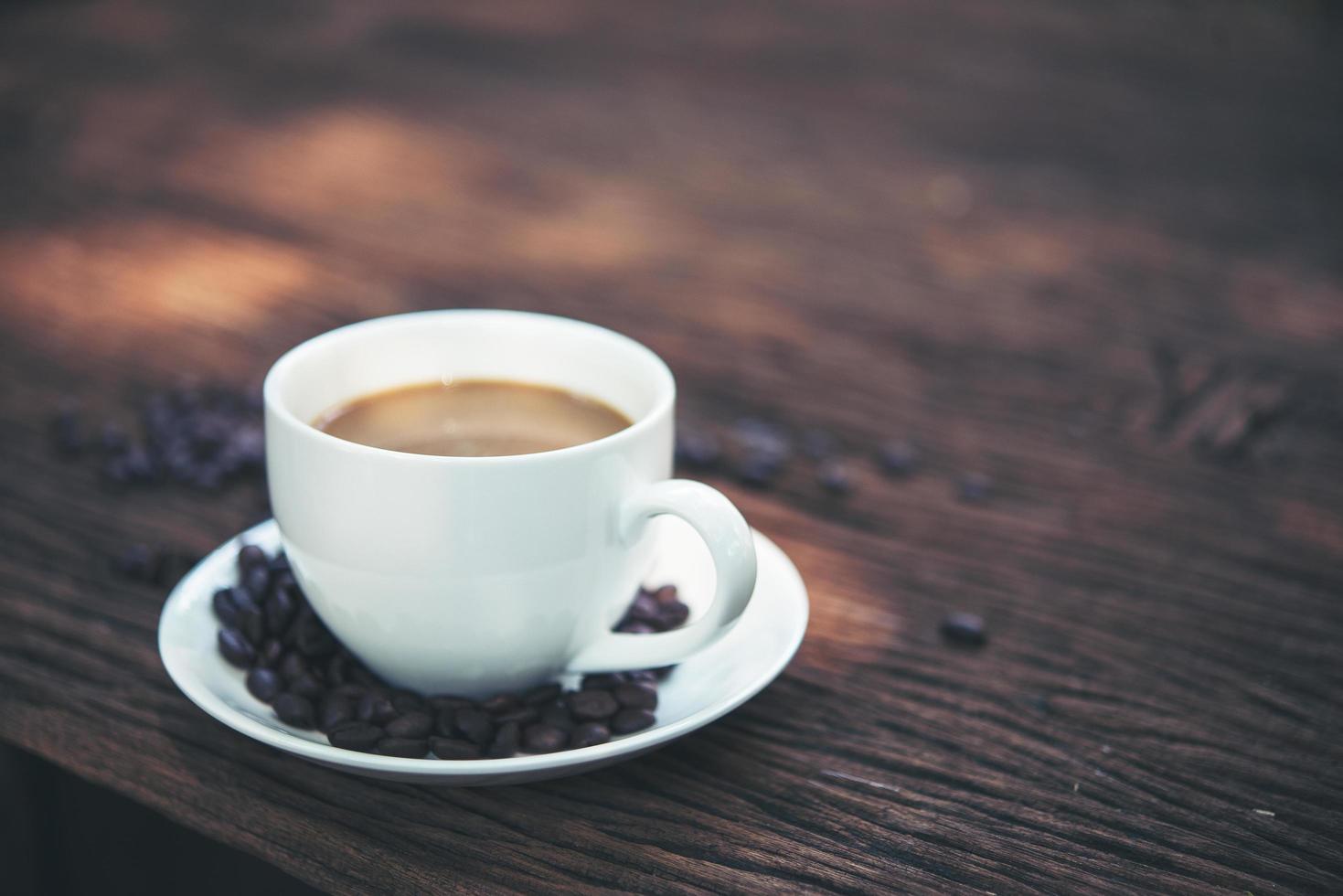 primo piano di una tazza di caffè con chicchi di caffè sul tavolo di legno foto