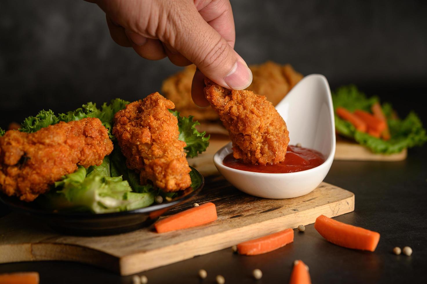 mano che immerge il pollo fritto croccante nella salsa foto