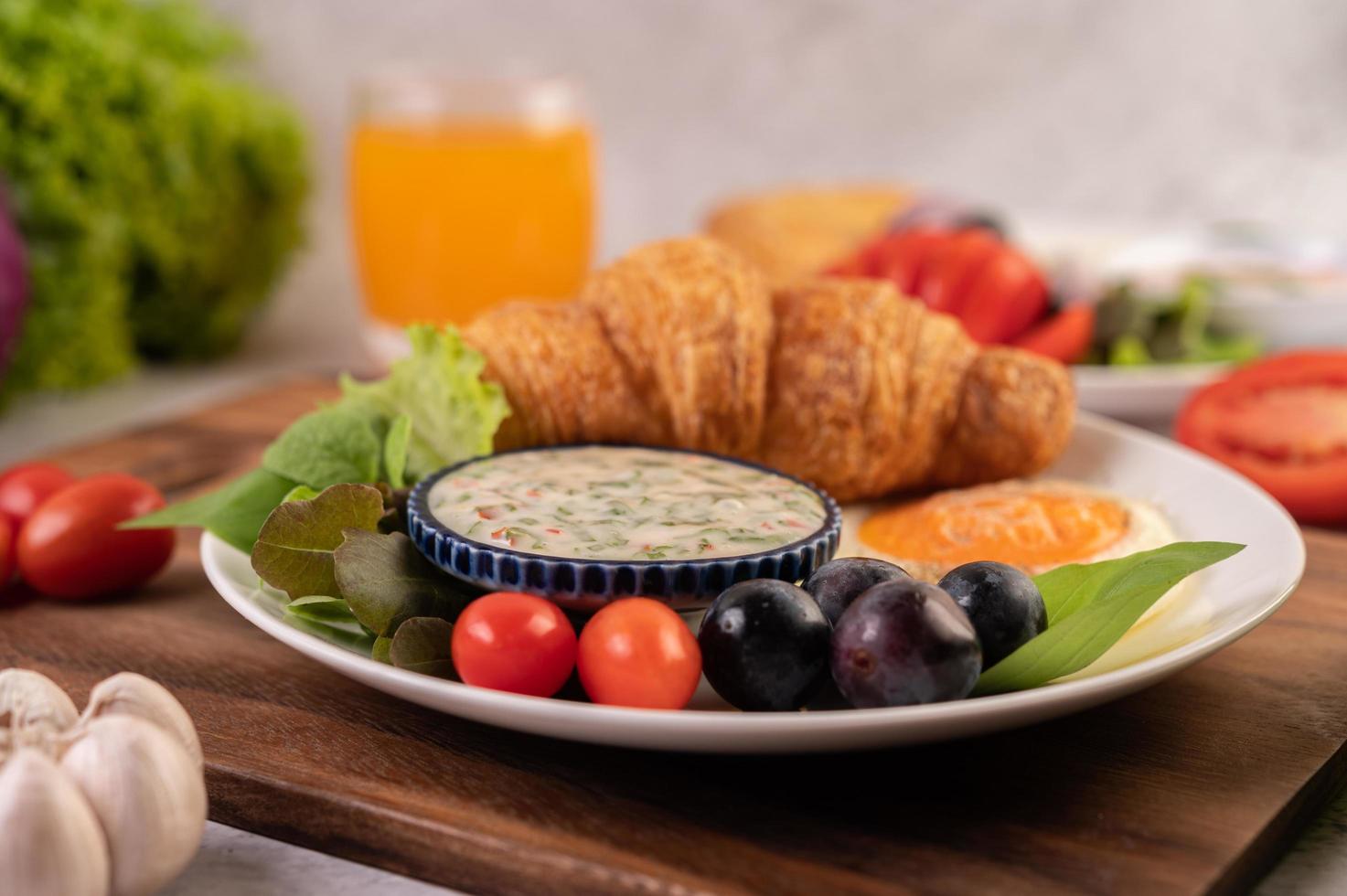 croissant, uovo fritto, condimento per insalata, uva nera e pomodori foto