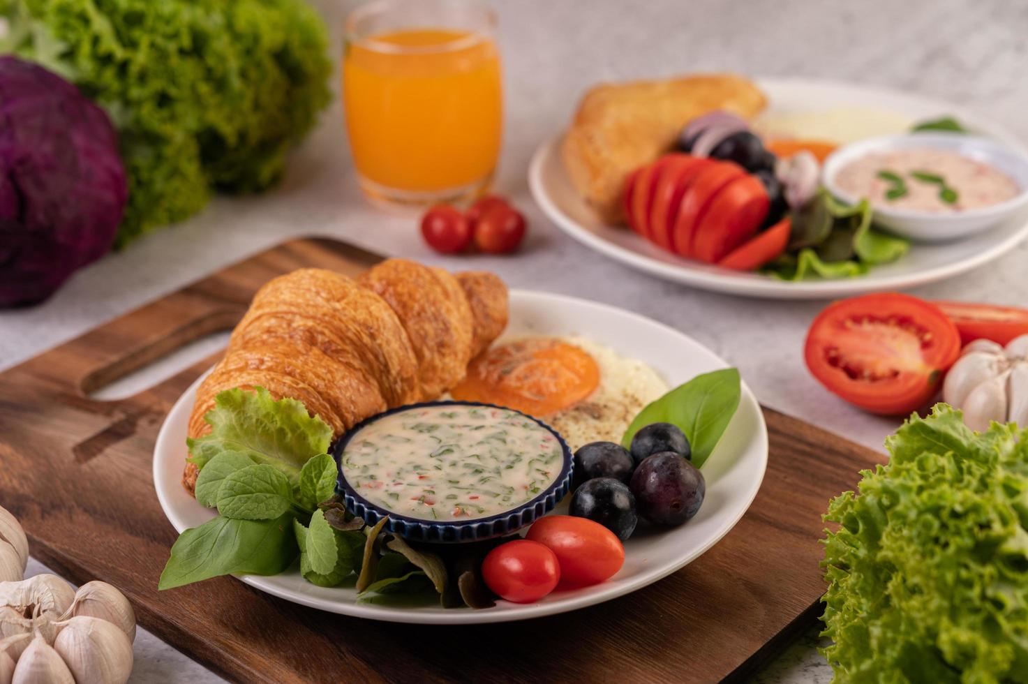 croissant, uovo fritto, condimento per insalata, uva nera e pomodori foto